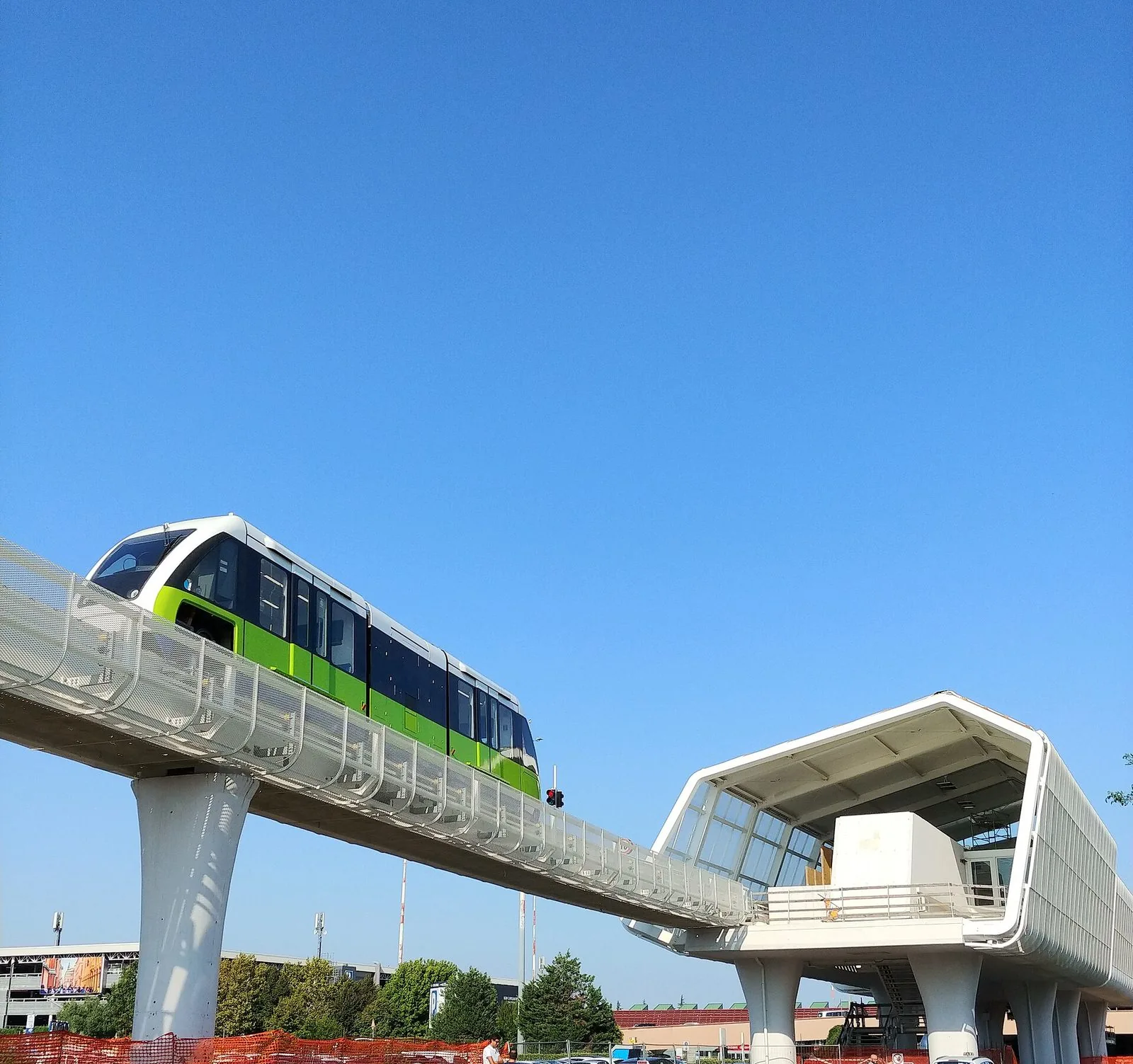 Il treno bianco e verde della monorotaia Marconi Express sul viadotto sopraelevato che entra nella stazione dell'aeroporto, sotto un cielo azzurro limpido